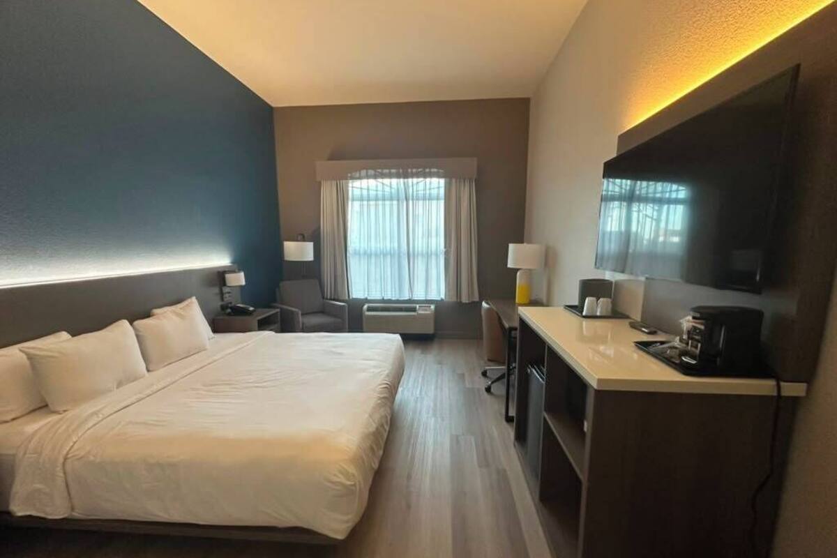 Ein Hotelzimmer mit Bett, Schreibtisch, Stuhl und einem großen Fenster mit Vorhängen.