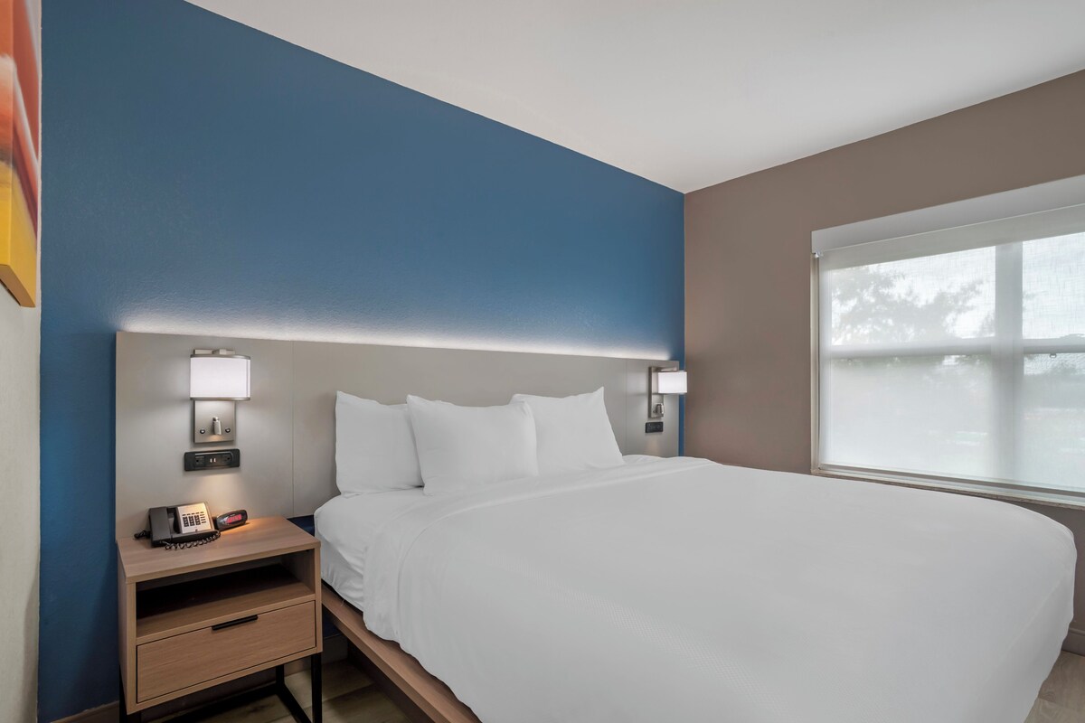 A hotel room with a bed, bedside tables, a lamp, and a window.