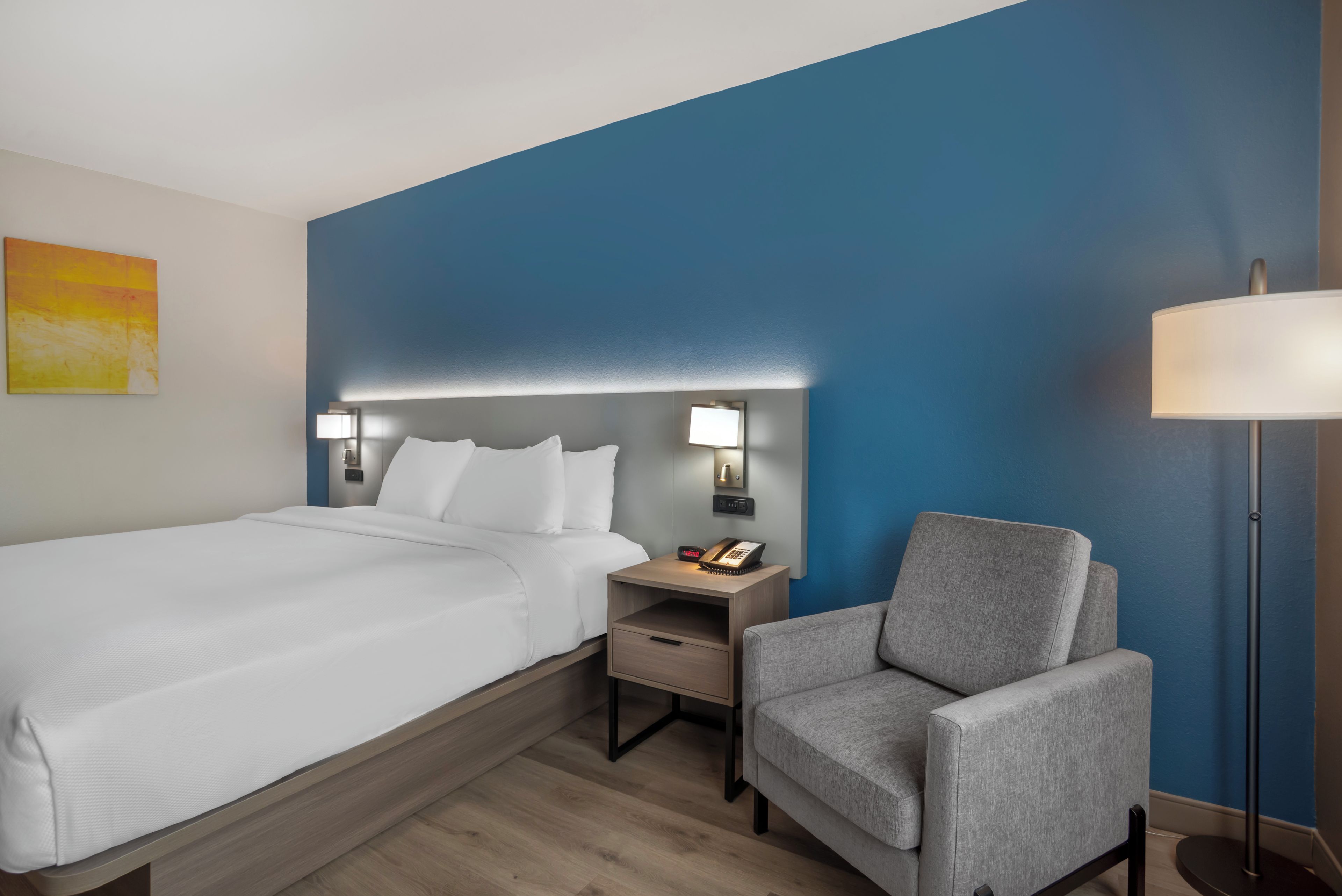 Una habitación de hotel con una cama, una mesita de noche con un teléfono, una silla y una lámpara.