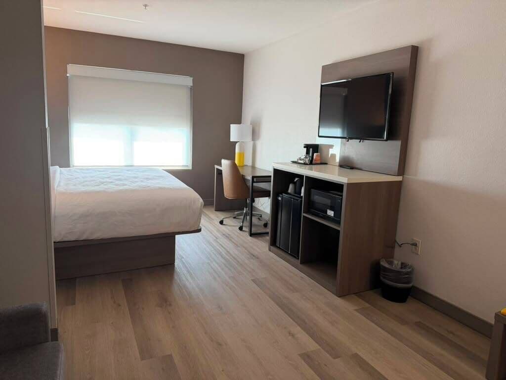 Una habitación de hotel con cama, escritorio, silla, televisor y ventana con persianas.