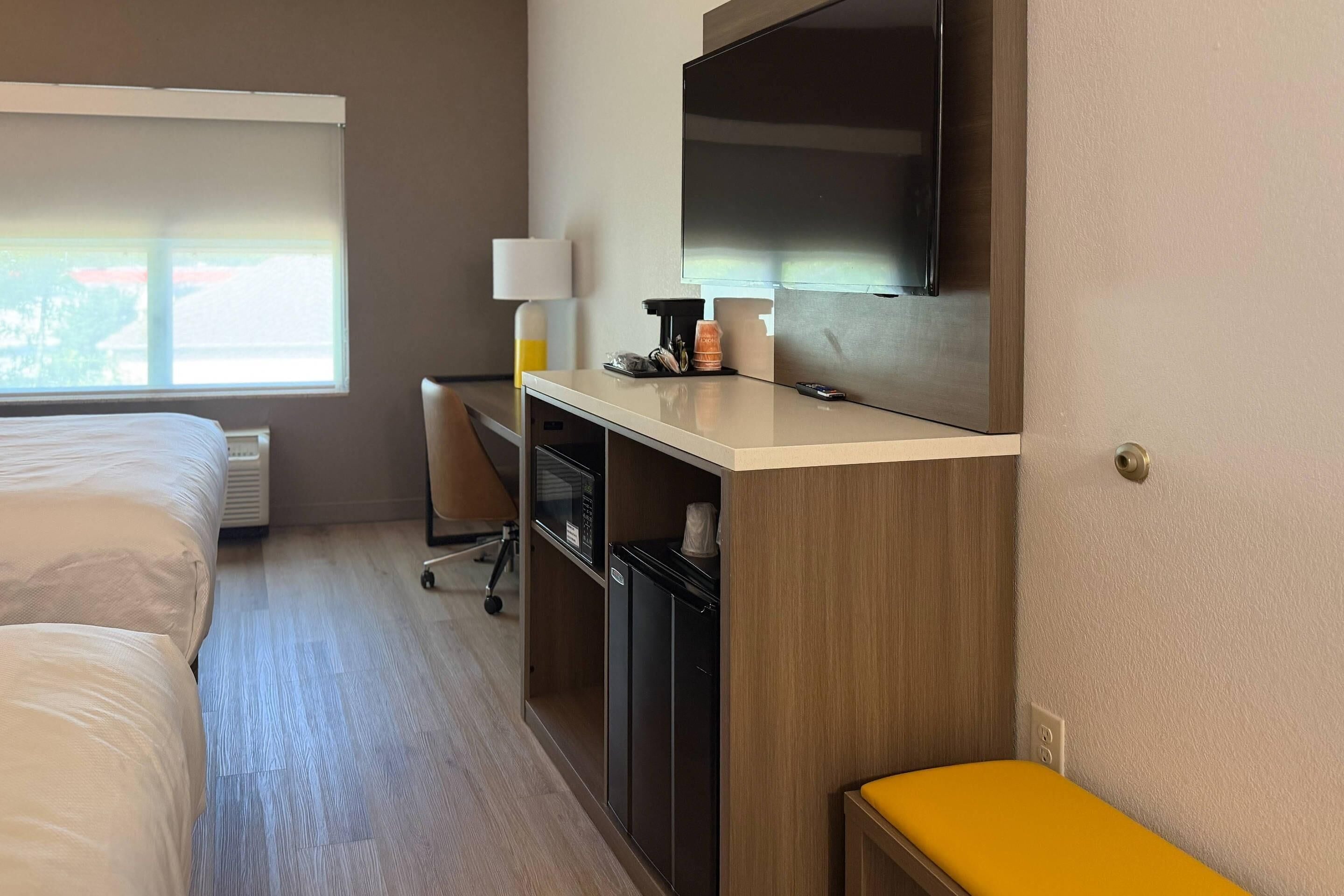 A hotel room with a bed, desk, TV, and a window with blinds.