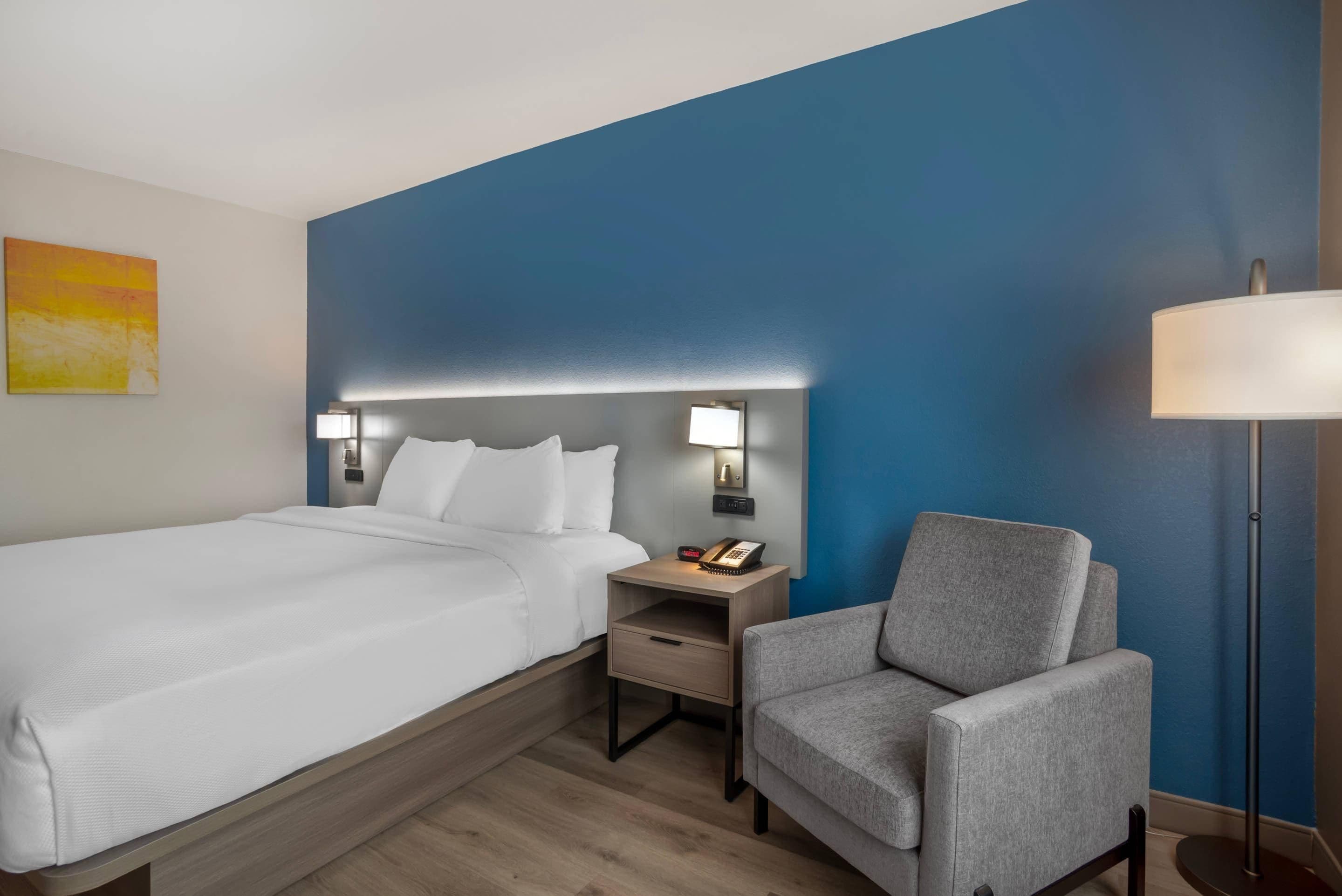 Een hotelkamer met een bed, nachtkastje, stoel en lamp.