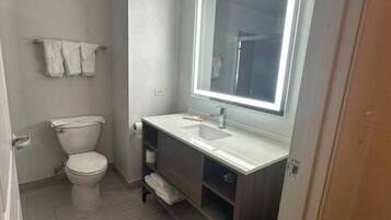 A small bathroom with a toilet, a sink, a mirror with built-in lighting, and a trash bin.