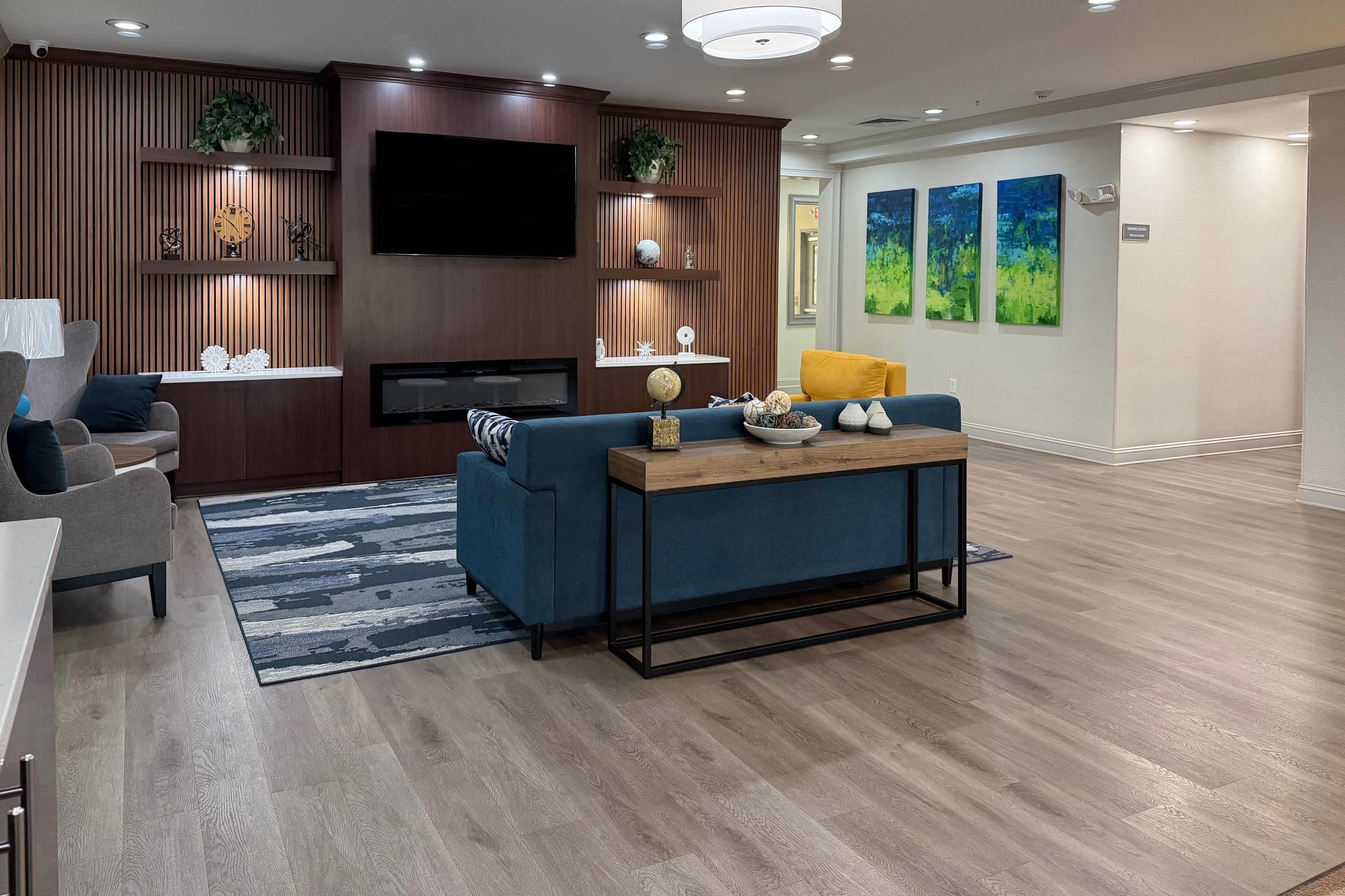 Un salón moderno con televisor de pantalla plana, un sofá azul, una mesa de centro de madera y una alfombra estampada.