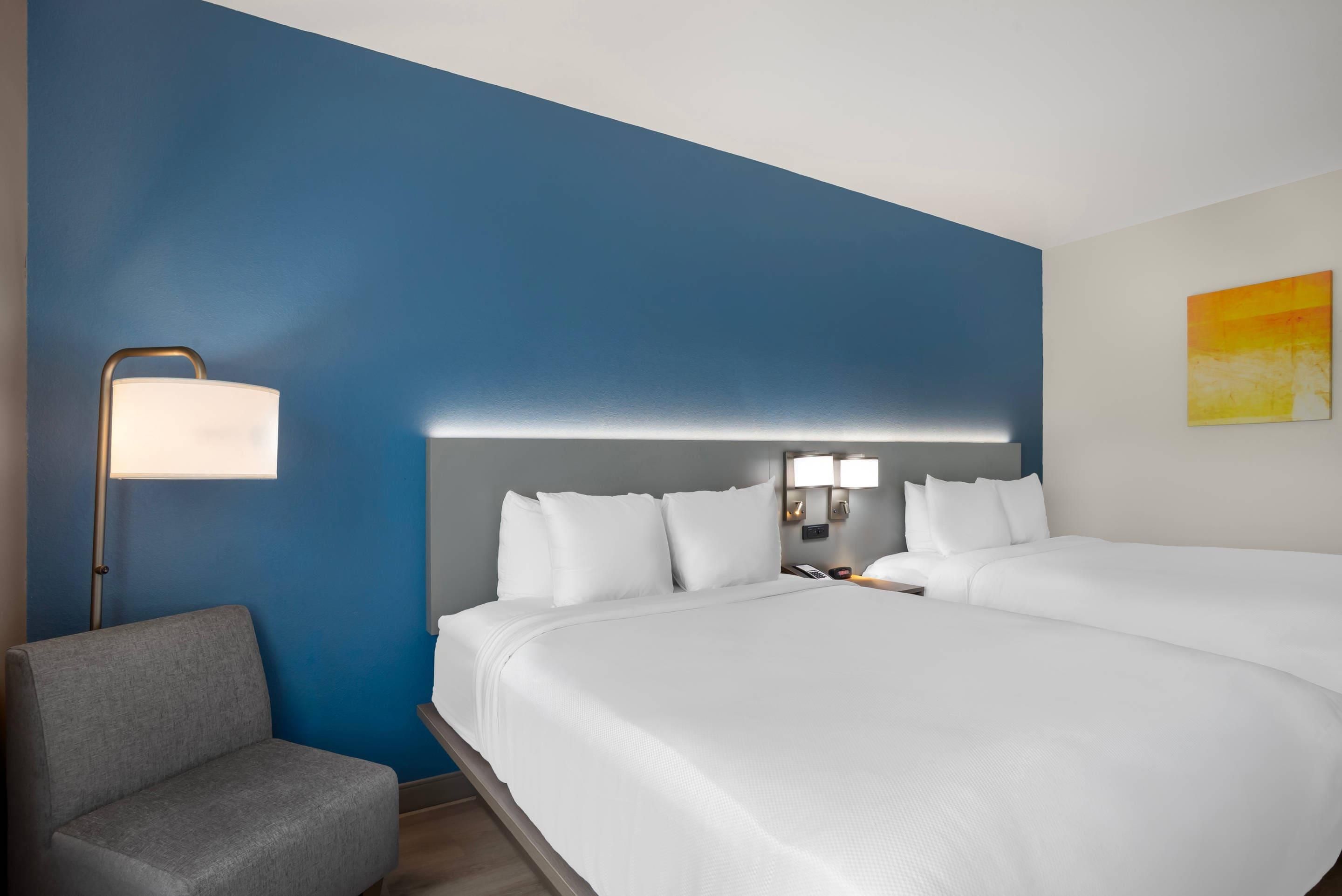 A hotel room with a large bed, a bedside table with a lamp, a chair, and a painting on the wall.