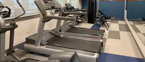 Une salle de sport équipée de tapis de course, d’une machine de musculation et d’un mur recouvert de miroirs.