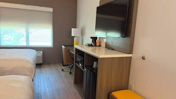 A hotel room with a bed, a desk with a computer, a TV, and a window with blinds.