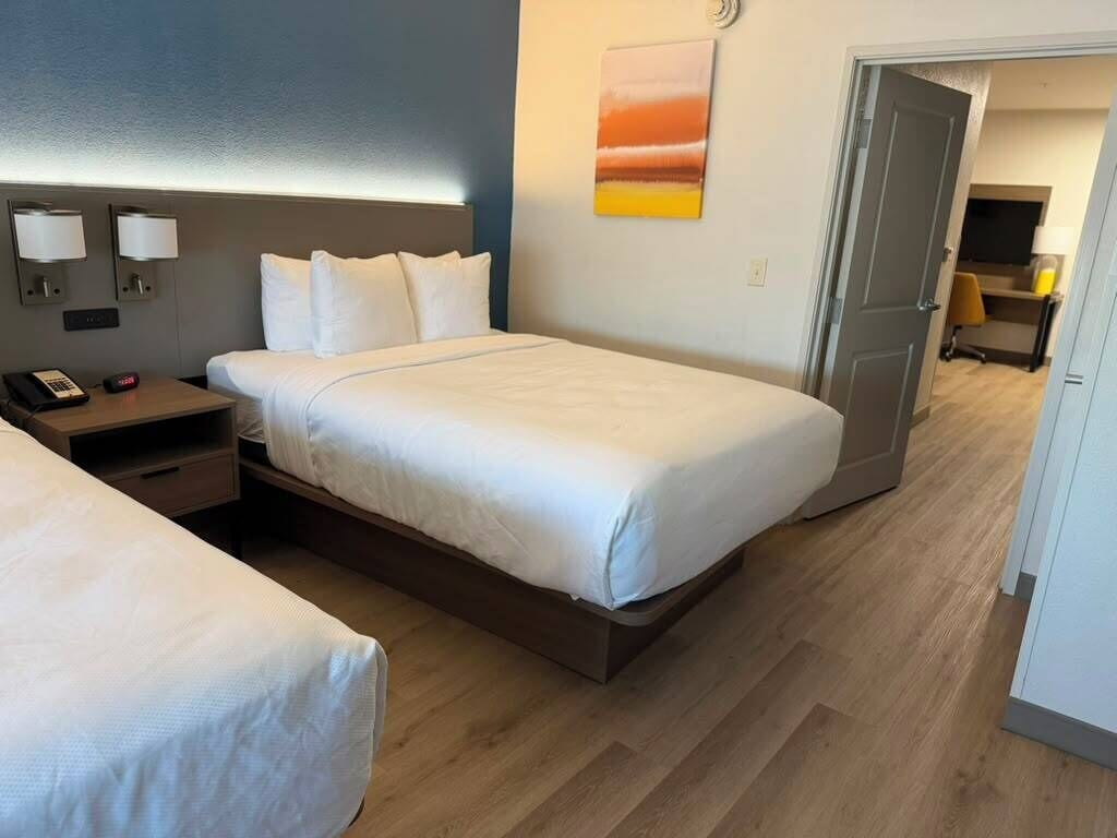 A hotel room with a bed, bedside tables, a desk, a chair, a TV, and a door.