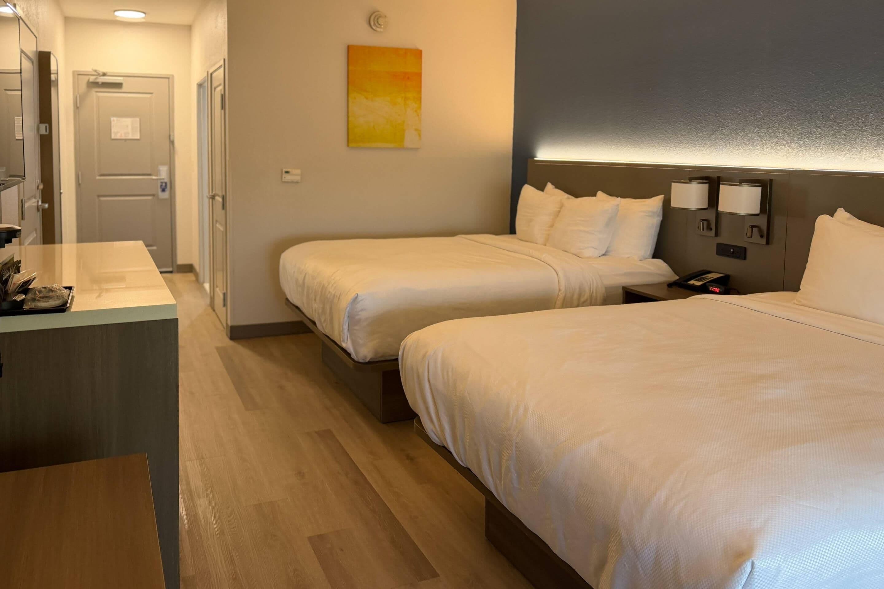 A hotel room with two beds, a bedside table, a desk, and a painting on the wall.