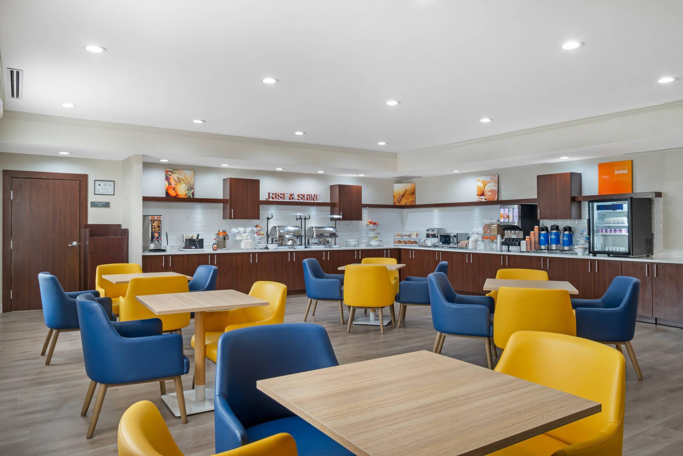 A modern dining area with yellow and blue chairs, a buffet counter, and a refrigerator.