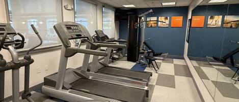 A gym with treadmills, elliptical machines, and a mirrored wall.