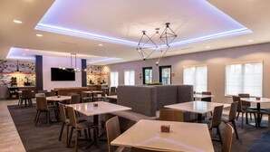 A modern dining area with multiple tables and chairs, a bar area, and a large seating area with a patterned wall. - La Quinta Inn & Suites by Wyndham Las Vegas Airport South (Las Vegas)