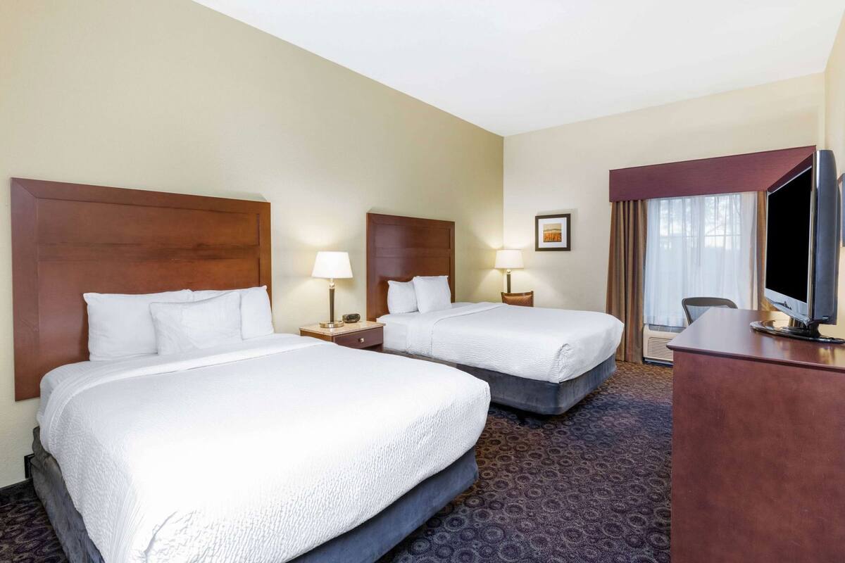 A hotel room with two beds, a desk, a TV, and a window with curtains.