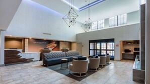 A spacious lobby with a modern design, featuring a seating area with sofas and armchairs, a reception desk, and a large window providing natural light. - La Quinta Inn & Suites by Wyndham Las Vegas Airport South (Las Vegas)
