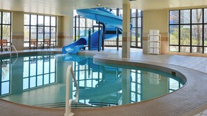 Una piscina con tobogán azul y escalones, rodeada por amplios ventanales.