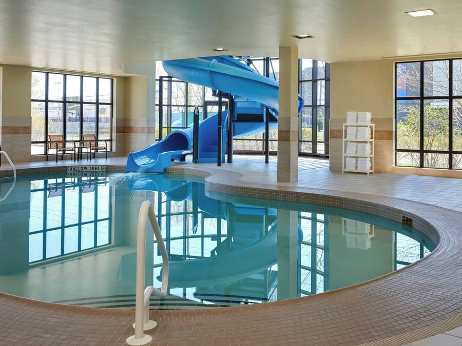 A swimming pool with a blue slide and stairs, surrounded by large windows.