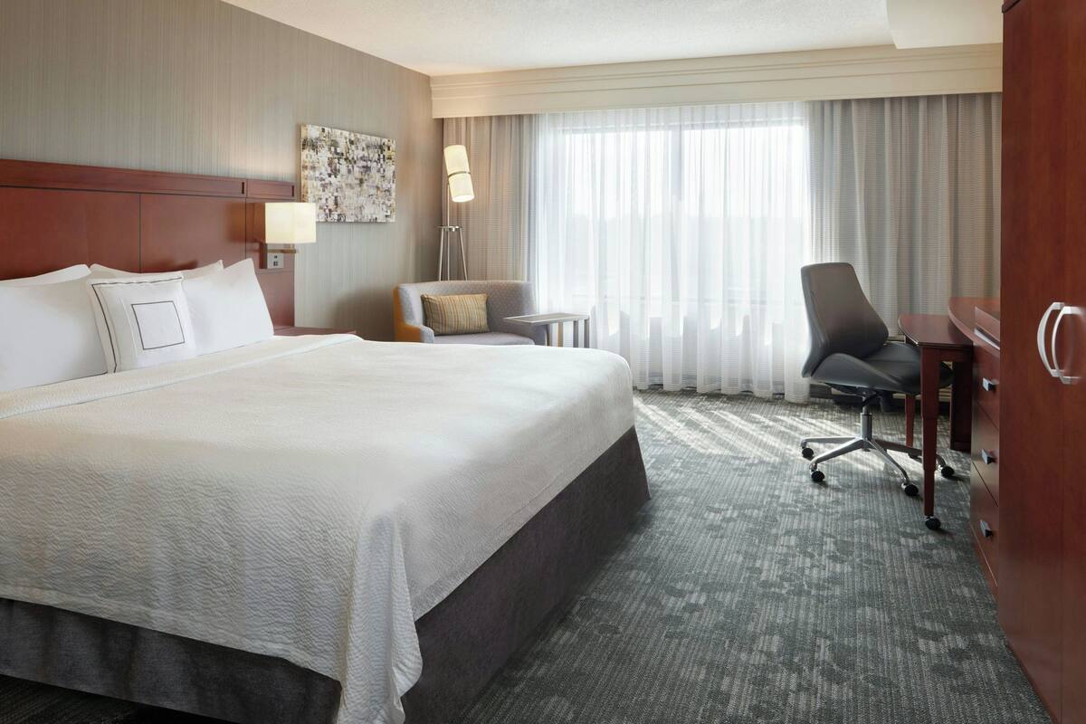 Una habitación de hotel con una cama grande, un escritorio, una silla y una lámpara.