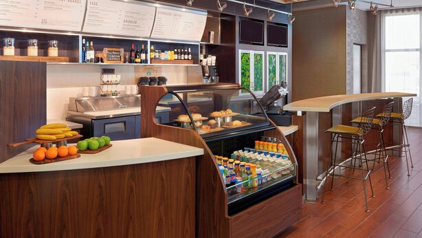Un café moderno con un mostrador que exhibe productos de desayuno, un refrigerador con alimentos y una pizarra con el menú.