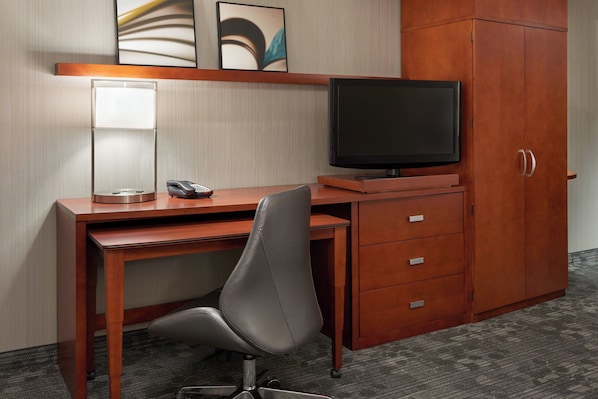 A hotel room with a wooden desk, a chair, a television, a telephone, and a cabinet.