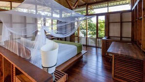 Una habitación con una cama bajo una mosquitera, muebles de madera y ventanas amplias.