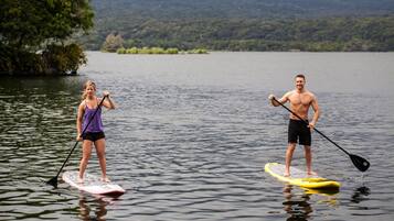 Two people paddleboarding on a calm lake with a forested mountain in the background.