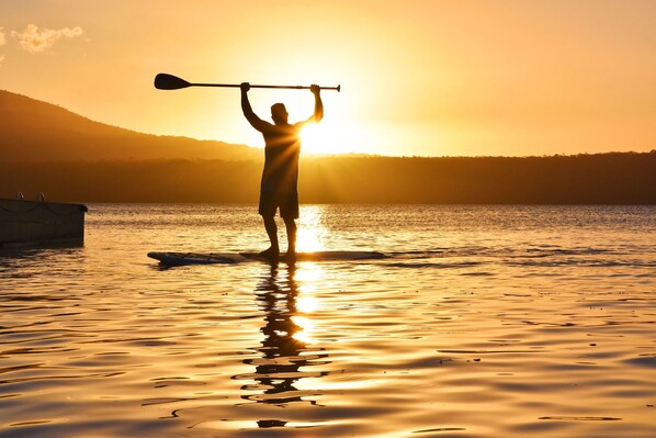 A person standing on a paddleboard holding a paddle, with a sunset in the background. - Jicaro Island Lodge Member of the Cayuga Collection (Granada)