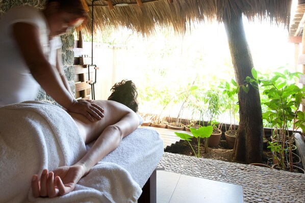 A person receiving a massage in a room with a thatched roof, potted plants, and a stone wall. - Jicaro Island Lodge Member of the Cayuga Collection (Granada)