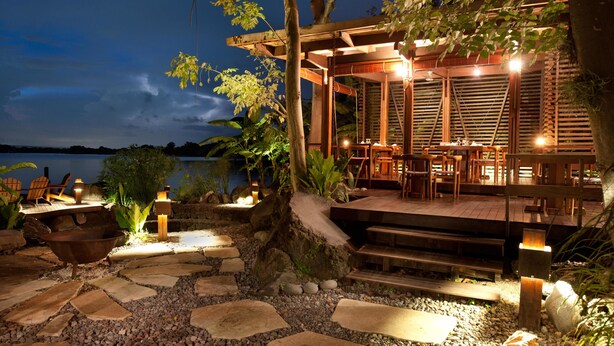 Una terraza de madera con mobiliario exterior, un camino de piedra y vista al agua.