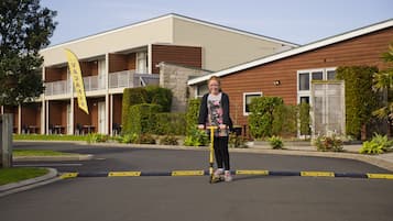 En person kører på en scooter på en vej foran en bygning med balkon og flag.