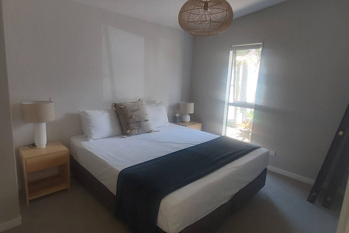 A bedroom with a bed, two bedside tables, a window, and a door.