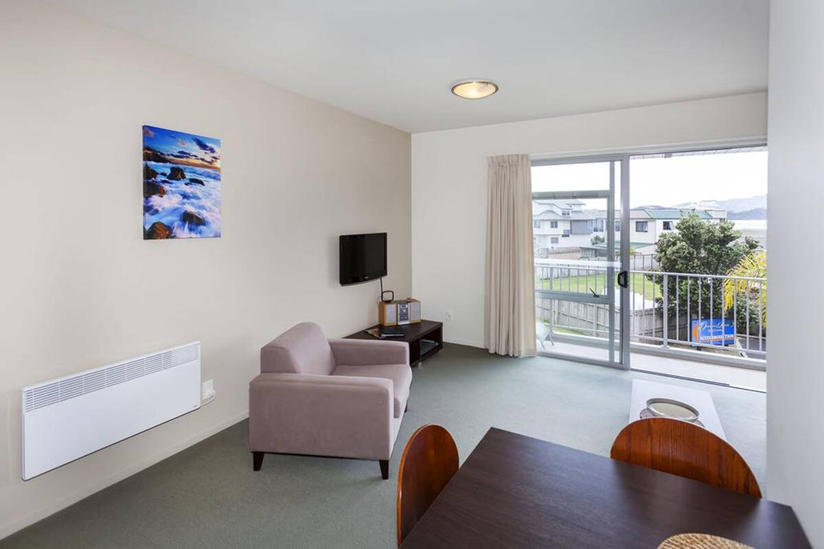 A modern hotel room with a large balcony, a flat-screen TV, a painting, and a dining area.