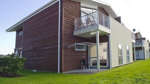 A modern two-story house with a balcony, a covered outdoor seating area, and a visible window.