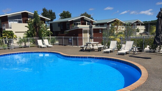 A swimming pool with a tiled edge, surrounded by lounge chairs and a fence.