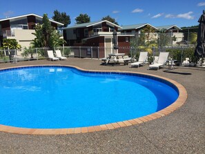 Una piscina con borde de baldosas, rodeada de sillas de descanso y una valla.