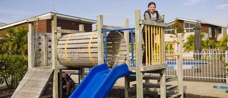 A playground with a blue slide, wooden climbing structures, and a yellow rope ladder.
