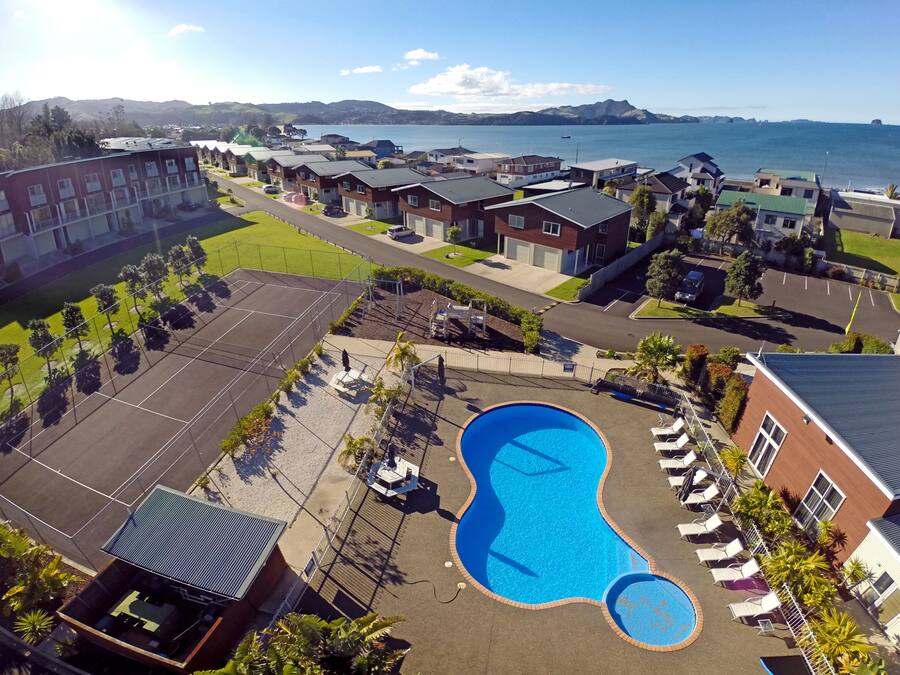 A residential area with a large swimming pool surrounded by lounge chairs and a view of the sea.