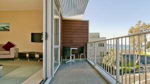 A balcony with a view of the sea, a sofa, a TV, and a table with chairs.