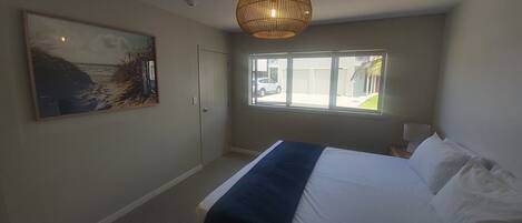 Ein Schlafzimmer mit Bett, einem Gemälde, einem Fenster und einer Tür.