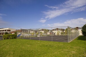 Cancha de tenis cercada con zona verde al frente, rodeada de edificios residenciales.