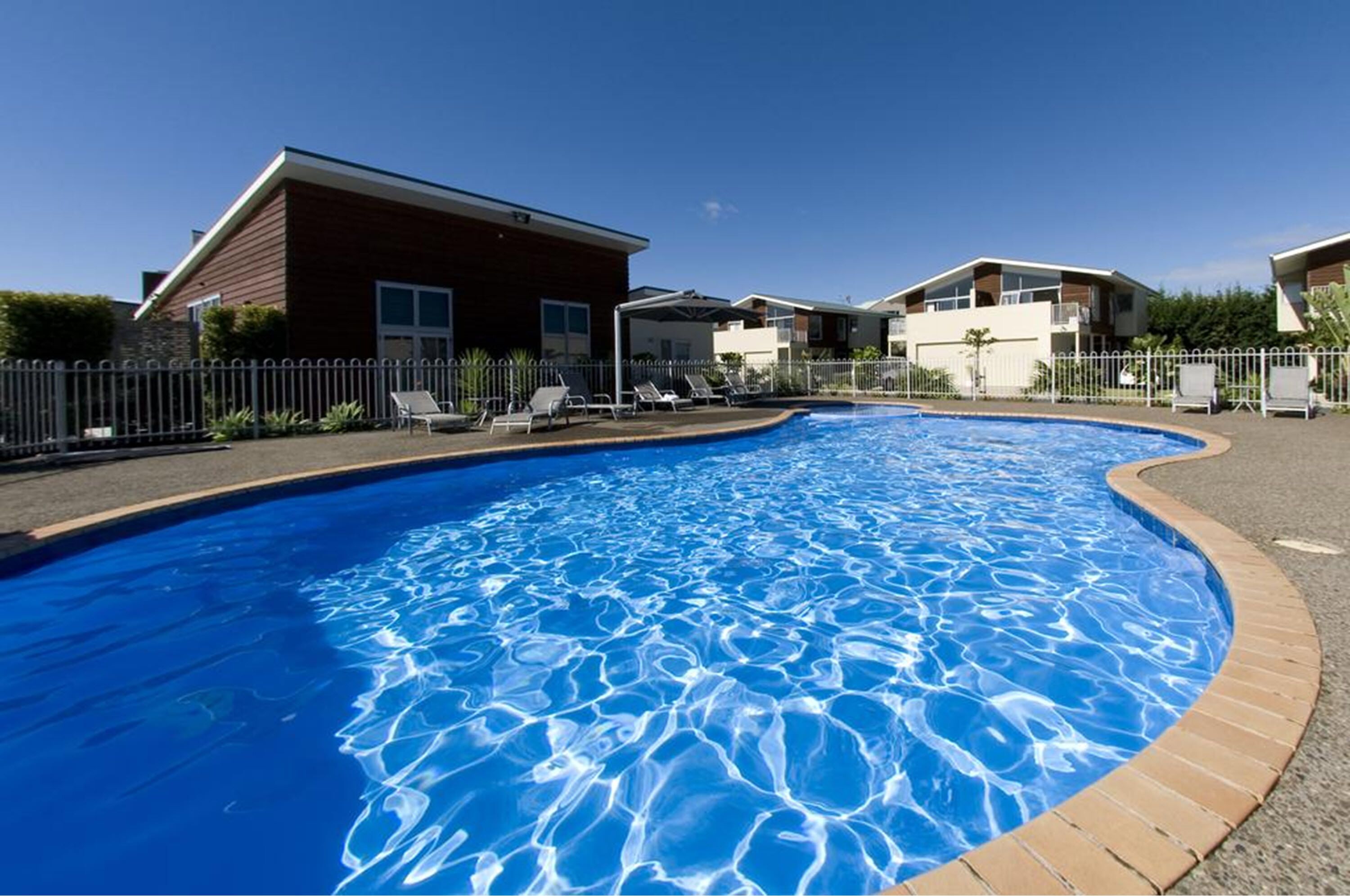 A swimming pool with lounge chairs and a fence, surrounded by buildings.