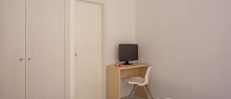 A bedroom with a bed, a desk with a computer, a chair, and a wardrobe.
