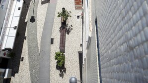 Une rue pavée bordée de bâtiments des deux côtés, avec une clôture et un panneau indiquant « FABRIQUÉ EN ».