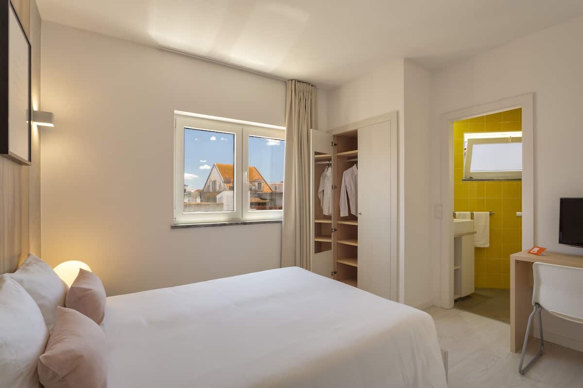 A hotel room with a bed, a desk, a wardrobe, and a bathroom visible through an open door.