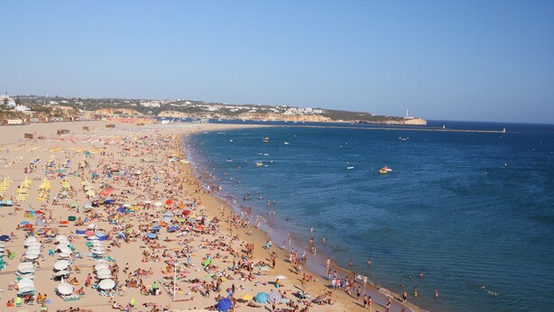 Une plage bondée, avec de nombreux parasols et beaucoup de monde.
