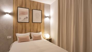 Een opgemaakt bed met twee kussens, een nachtkastje met een lamp, en twee ingelijste foto's aan de muur.