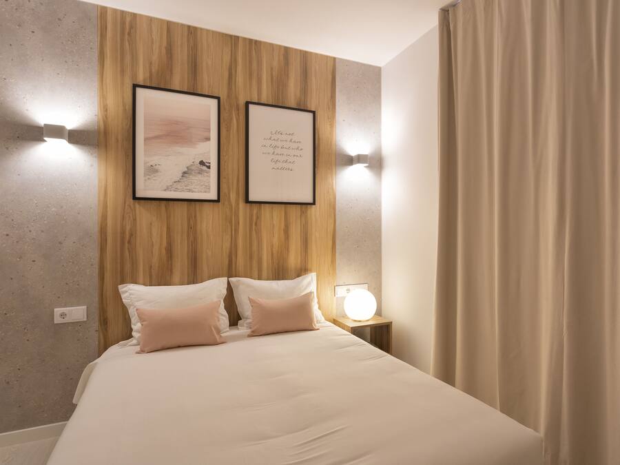 Een opgemaakt bed met twee kussens, een nachtkastje met een lamp, en twee ingelijste foto's aan de muur.