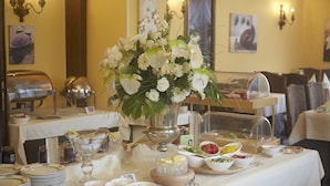 A buffet setup with various food items, a floral centerpiece, and dining tables.