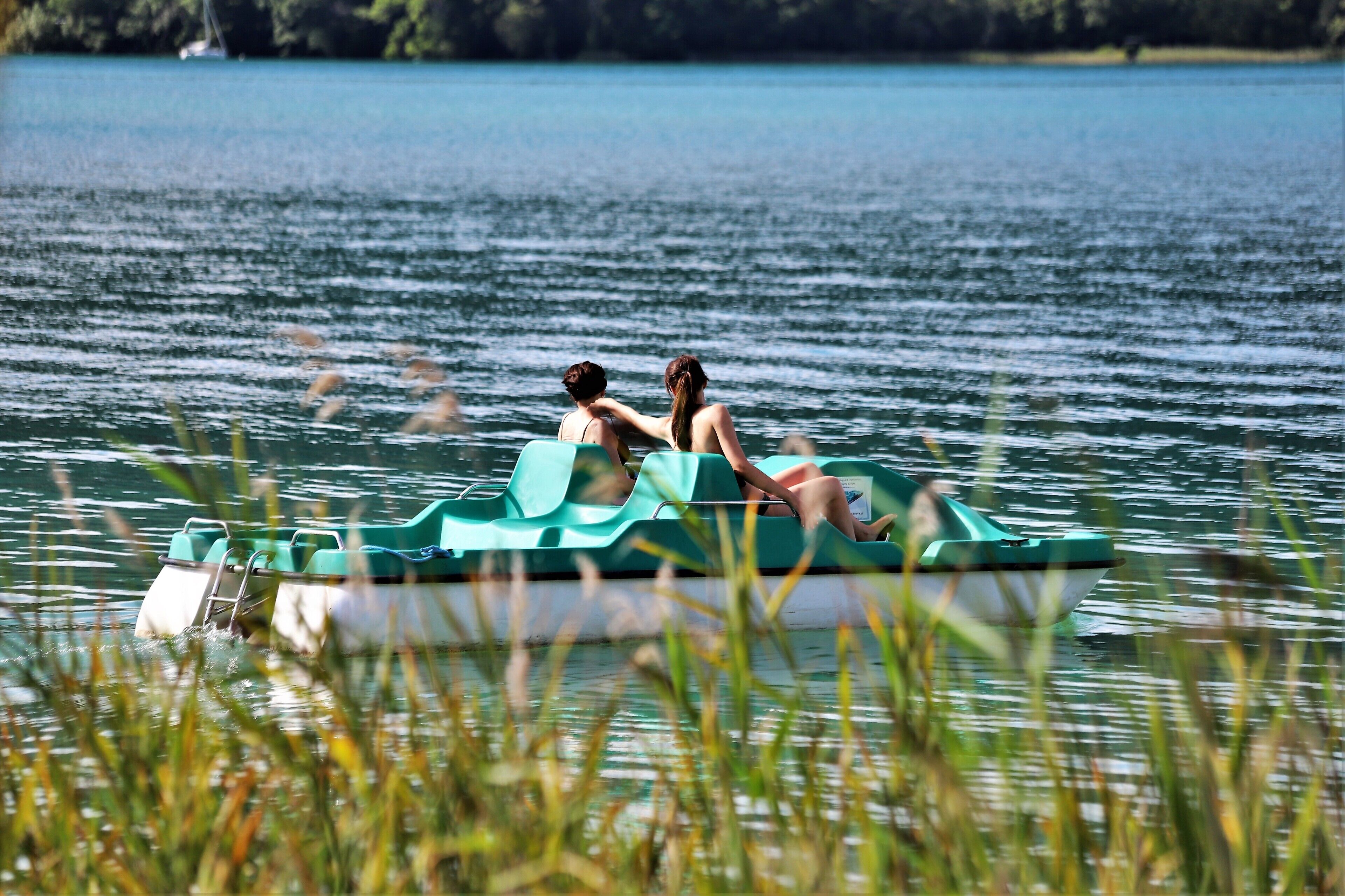 A green boat with two people on it, floating on a calm lake.
