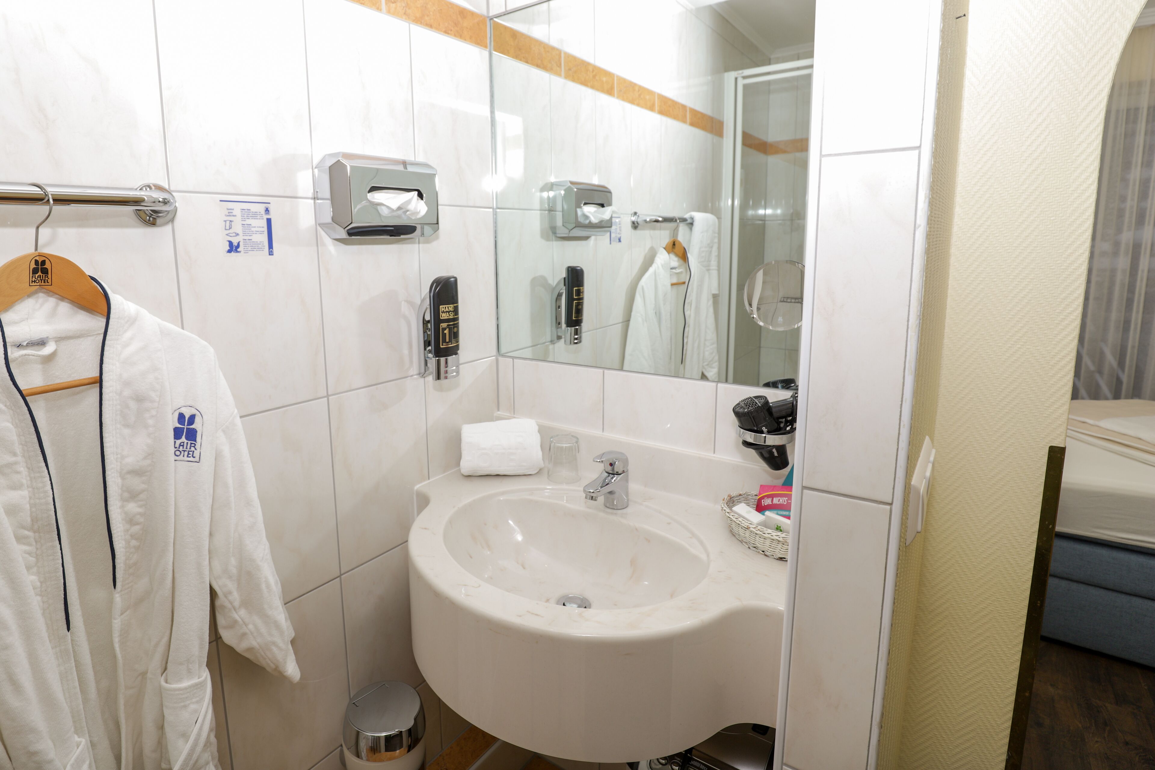 Ein Badezimmer mit Waschbecken, Handtuchhalter, Handtrockner und Spiegel.