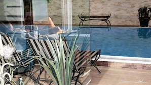 A glass-enclosed swimming pool with a view of a brick wall and a bench.